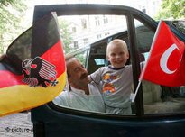 Türkischer Vater mit Kind vor deutscher und türkischer Nationalfahne; Foto: dpa