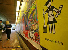Passanten schauen in einer Tunnelunterführung auf ein Plakat mit einem Piktogramm von Migrantas; Foto: dpa