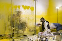 Der Künstler versucht im Sitzen zu essen, während eine Besucherin sicher hinter einer Glaswand sitzt. Foto: Wafaa Bilal