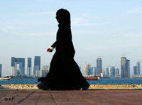 إمرأة محجبة تمر قرب أحد شواطئ الدوحة وتظهر خلفها عمارات الدوحة شاهقة الارتفاع 