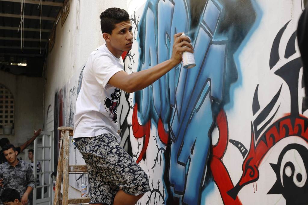 Junger Graffiti-Künstler vor seinem Wandgemälde an einer zerbombten libyschen Militärbasis; Foto: Valerie Stocker