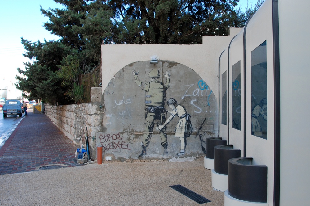 Ein israelischer Soldat wird von einem jungen Mädchen abgetatstet - Graffiti von Bansky aus dem Jahr 2007; Foto: Laura Overmeyer