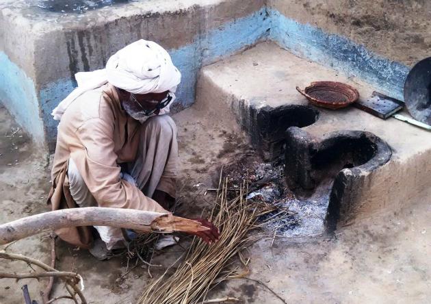 An elderly man prepares to light a fire in an outdoor hearth (photo: Usman Mahar) 