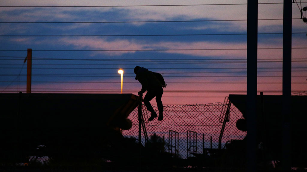 Ein Flüchtling klettert über einen Zaun in der Nähe der Eisenbahnschienen am Eurotunnel. Foto: picture-alliance/ empics/ Y. Mok