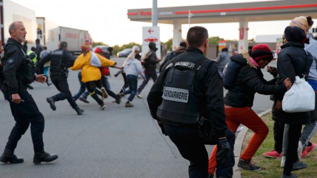French police officers chase migrants away from a closed petrol station, which was used as a meeting point for those wishing to cross the Channel Tunnel to England (photo: Reuters/P. Rossignol)