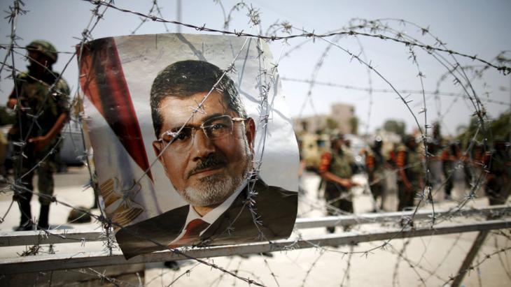 Poster of Morsi in front of a barbed wire fence erected by the military in Cairo (photo: picture-alliance/dpa/K. Elfiq)