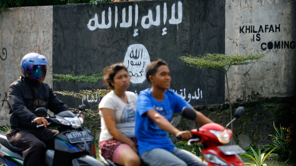 شاب يقود دراجته النارية وخلفه امرأة وعلى الحائط رمز تنظيم "الدولة الإسلامية" إندونيسيا.  (photo: picture-alliance/AP)