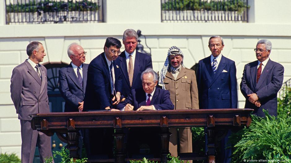 Minister of Foreign Affairs of Israel Shimon Peres puts his signature on the agreement during the signing ceremony of the historic Israeli-PLO Agreement, known as the Oslo 1 Accord, on the South Lawn of the White House in Washington, DC on September 13, 1993. Pictured, from left to right: Foreign Minister Andrei Kozyrev of Russia; Prime Minister Yitzhak Rabin of Israel; unknown aide; United States President Bill Clinton; Peres; Chairman Yasser Arafat of the Palestine Liberation Organisation (PLO); U.S. Secretary of State Warren Christopher; and Arafat aide Mahmoud Abbas (photo: picture-alliance/dpa/A. Sachs)