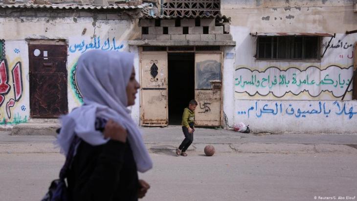 Wessal Abu Amra geht auf ihrem Nachhause-Weg von der Schule an einem spielenden Jungen vorbei; Foto: Reuters/Samar Abo Elouf