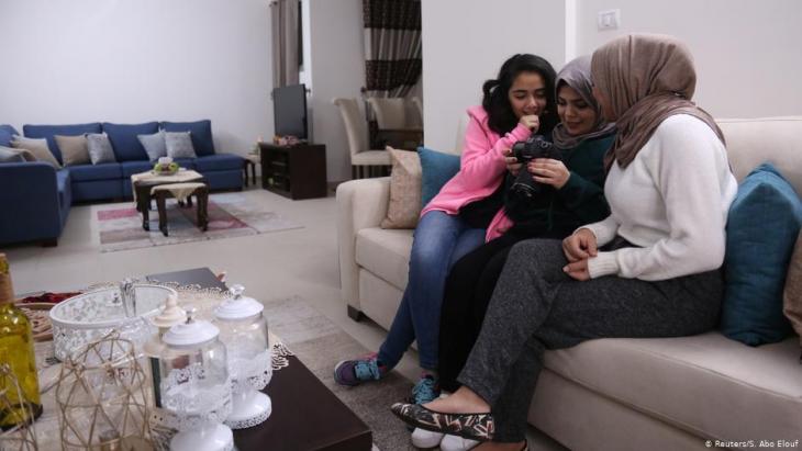 Die 27jährige Nada Rudwan (m.), Absolventin der Englischen Fakultät, schaut Videos von ihr, die von ihrer 22jährigen Schwester Lama Rudwan (r.), beim Kochen in ihrem Haus in Gaza City aufgenommen wurden; Foto: Reuters/Samar Abo Elouf