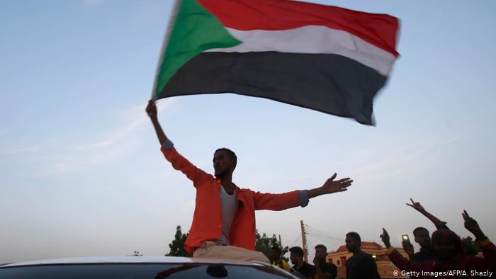 A man waves the Sudanese flag from atop a car (photo: Getty Images/AFP/A. Shazly)