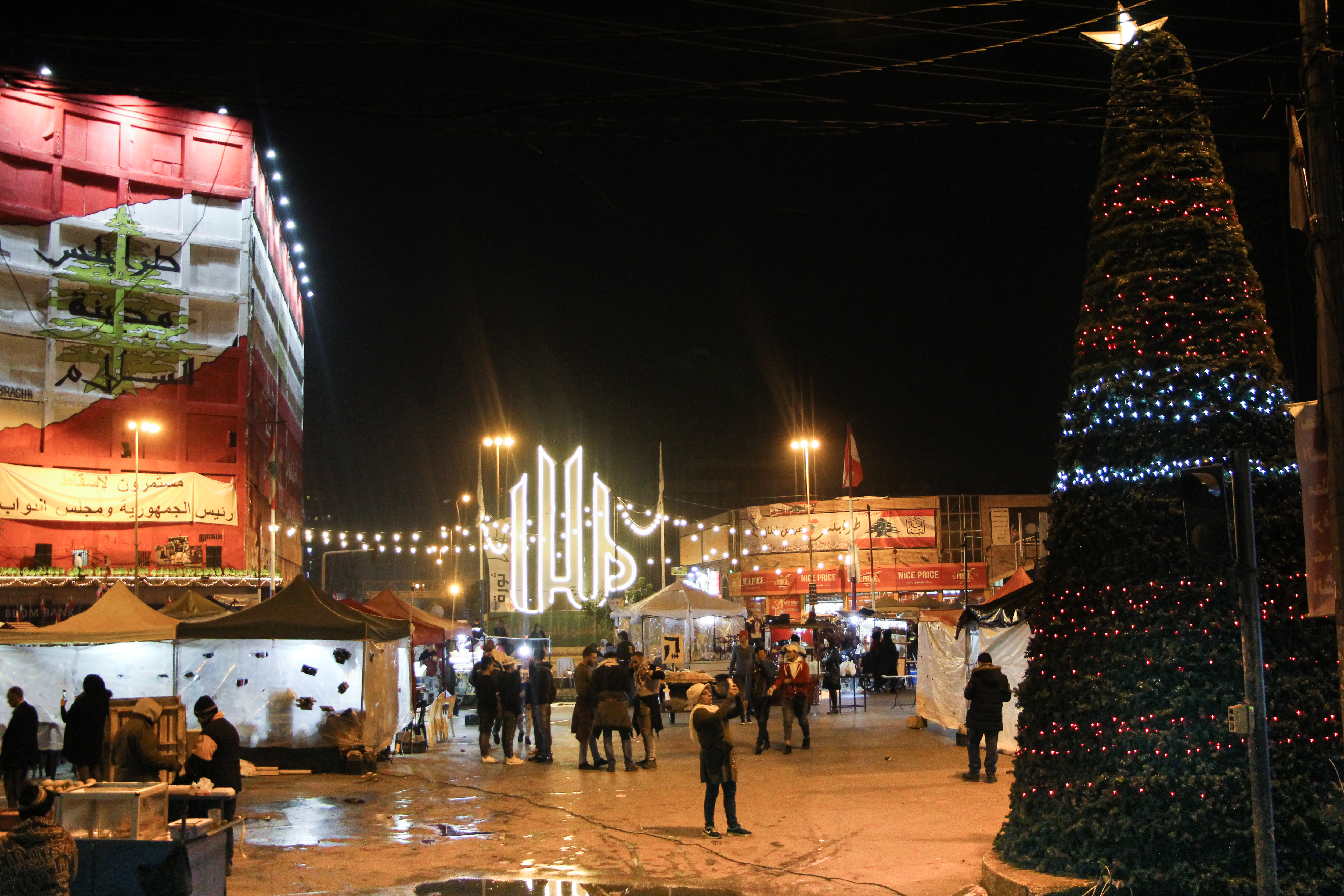 بمدينة طرابلس اللبنانية شجرة عيد الميلاد في ساحة النور، بجانب كلمة "الله" المكتوبة بحروف كبيرة مضاءة بألوان زاهية. Foto: Hanna Resch