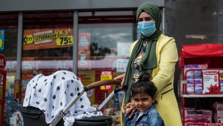 Eine Frau mit Kopftuch und Corona-Maske schiebt ihren Kinderwagen, an der Hand ein weiteres Kind; Foto Sanne Derks