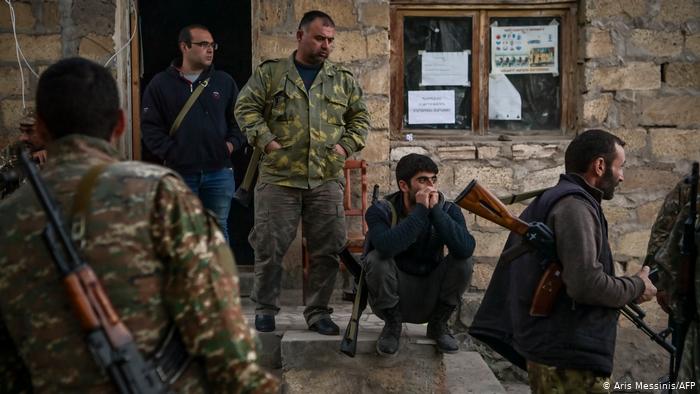 Several men, some wearing camouflage shirts, squatting and standing in front of a building in Stepanakert (photo: Aris Messinis/AFP)