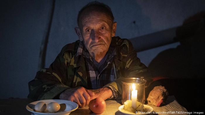 An elderly man in the dark, seated a table with a lit candle and plates with boiled eggs, a tomato, bread (photo: Stanislav Krasilnikov/ITAR-TASS/imago images)