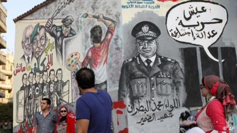 Herbst 2012: Eine ägyptische Frau trägt ihr Baby an einem Wandbild auf einer kürzlich weiß getünchten Wand vorbei, während andere in der Nähe Fotos machen, Tahrir-Platz, Kairo, Ägypten. Die arabische Schrift in der Gedankenblase lautet: "Es lebe die Freiheit, soziale Gerechtigkeit! Foto: AP-Foto/Mohammad Hannon