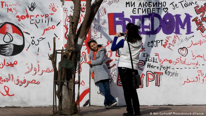 Young women take pictures of themselves standing in front of graffiti-filled walls (photo: picture-alliance/AP Photo/Ben Curtis)