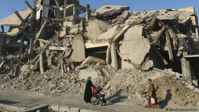 Photo from Abood Hamam shows a woman pushing a stroller through rubble