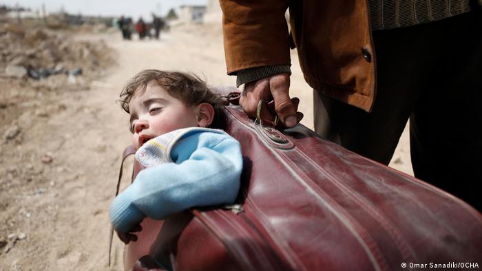 Omar Sanadiki captures a man pulling a child in a suitcase as people flee Ghouta in 2018