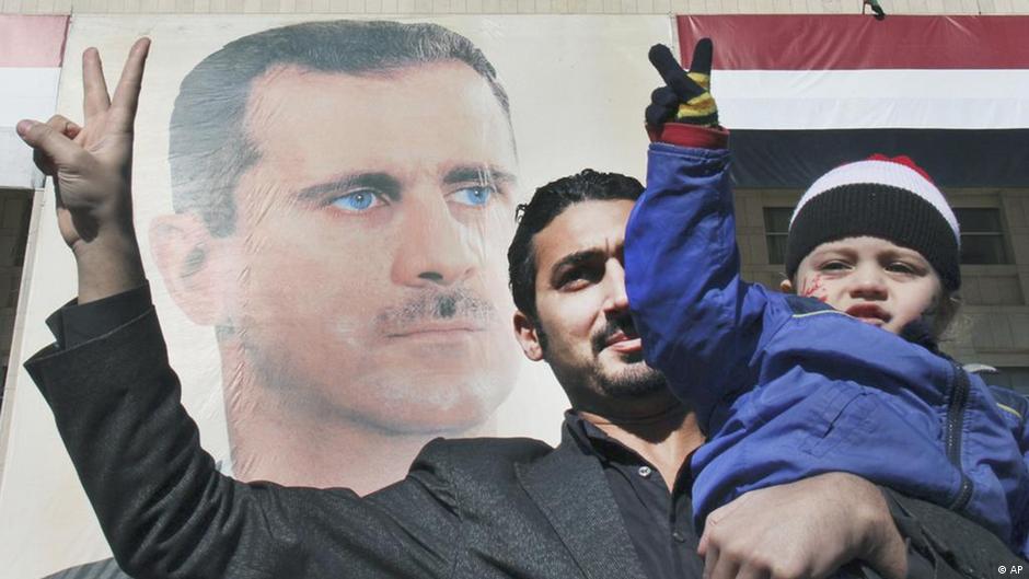 Ein Pro-Regime-Demonstrant hält seinen Sohn hoch während er das Victory-Zeichen vor einem riesigen Porträt des syrischen Präsidenten Bashar Assad zeigt, um seine Solidarität für ihn zu beweisen, Syrien, 20, Januar 2102