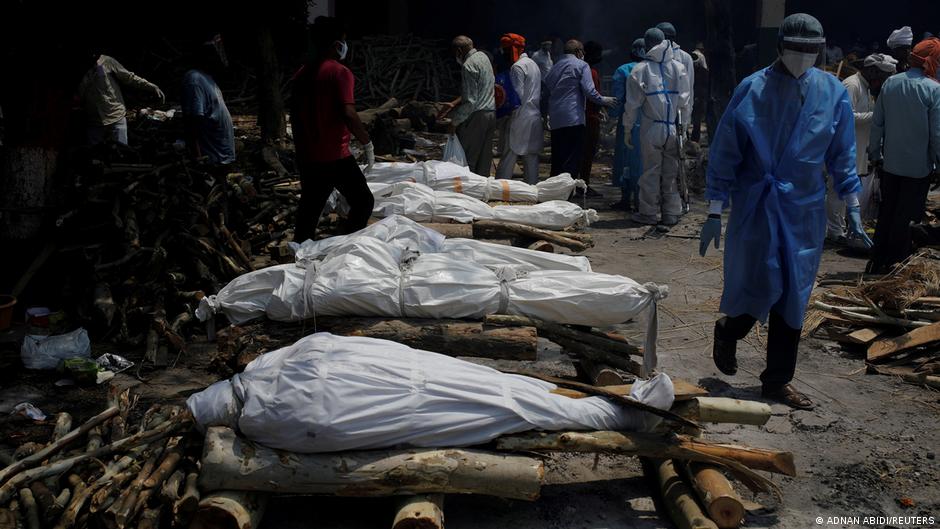 A health worker wearing personal protective equipment (PPE) walks past the funeral pyres of those who died from the coronavirus disease (COVID-19) during a mass cremation at a crematorium in New Delhi, India, 26 April 2021 (photo: REUTERS/Adnan Abidi)