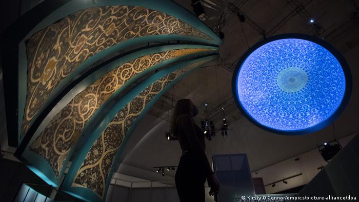 Eine Museumsmitarbeiterin betrachtet eine hellleuchtende blaue Projektion an der Decke.