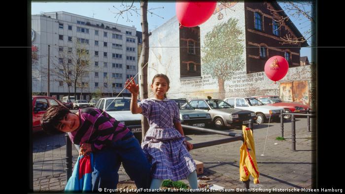 Two children with balloons in front of a parking lot