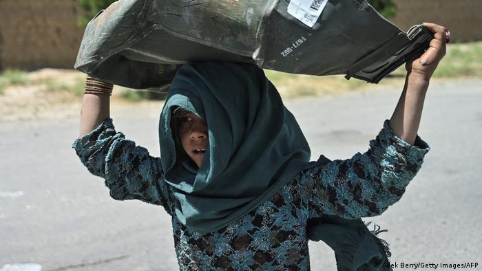 Ein Mädchen holt eine zerbeulte Metallkiste vom Schrottplatz in Bagram