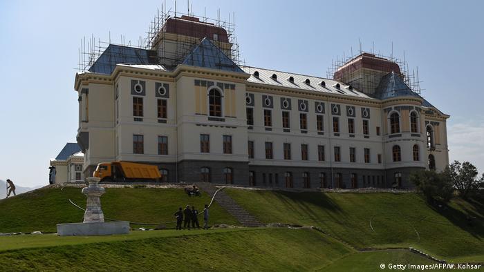 A grand building sits on a small hill with scaffolding its roof