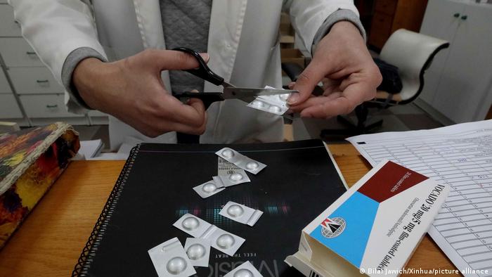 A chemist cuts blister pack medication into strips for rationing.