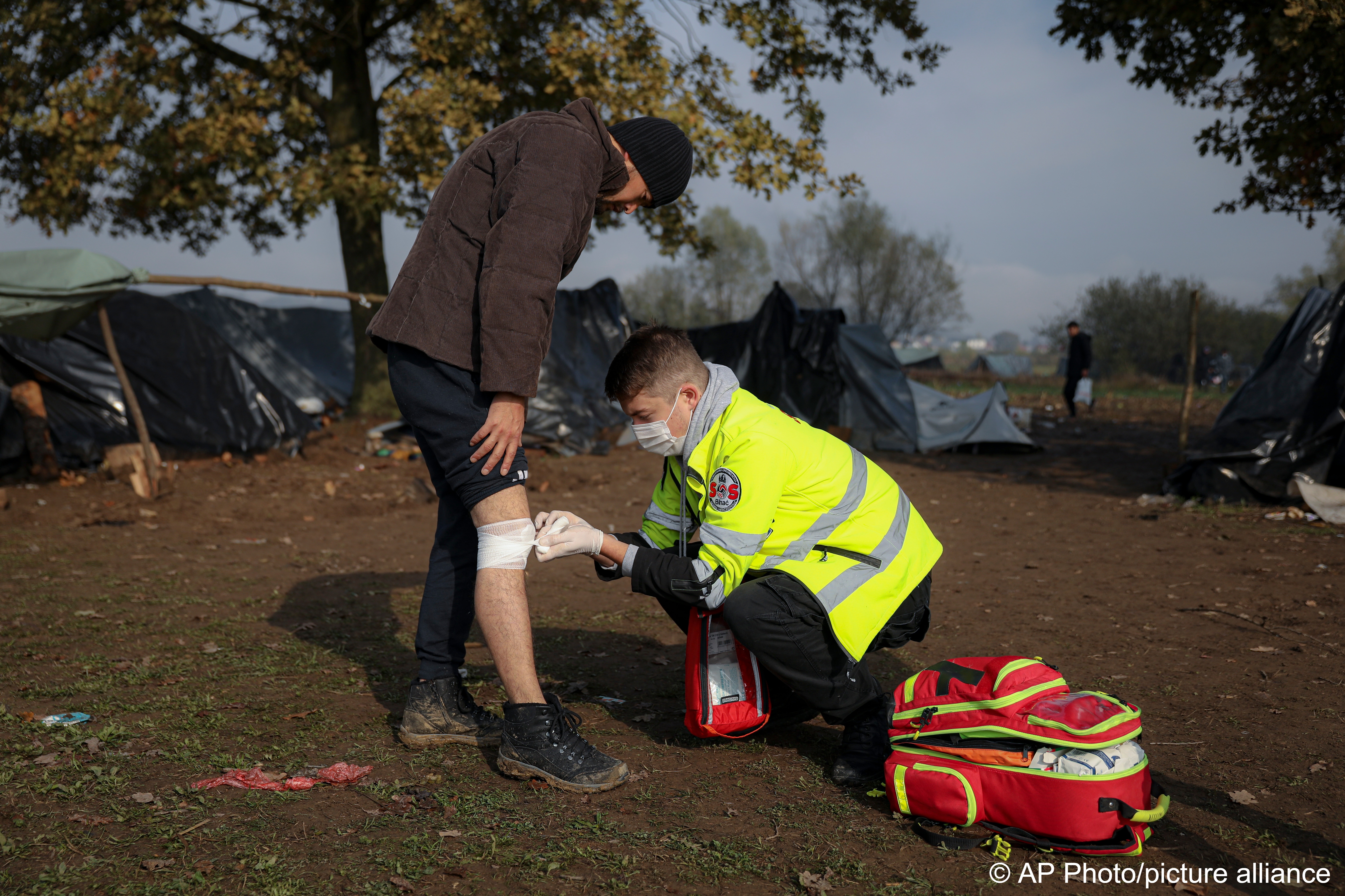 Ein Freiwilliger der NRO SOS Bihac kümmert sich um einen verletzten Migranten in einem Behelfslager für Migranten, die hauptsächlich aus Afghanistan stammen, in Velika Kladusa, Bosnien, 12. Oktober 2021; Foto: AP Photo