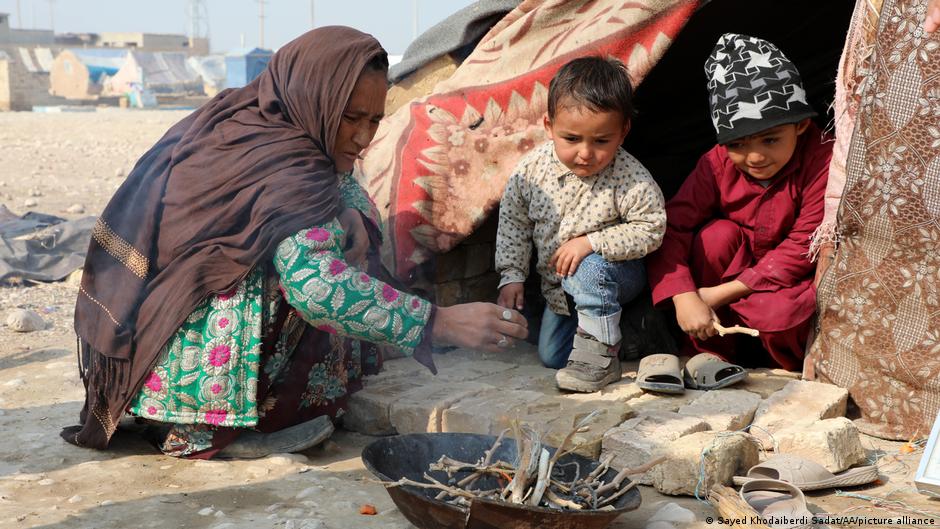 A woman and two children watch a small fire outside a tent (photo: Sayed Khodaiberdi Sadat/AA/picture alliance)