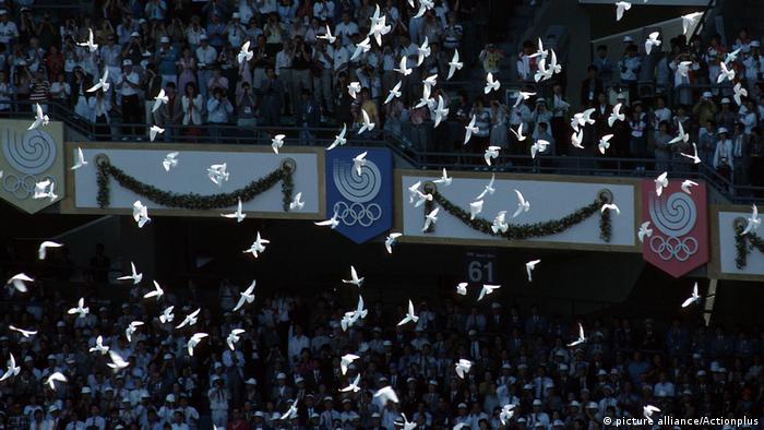 Bei den Olympiaspielen fliegen Tauben über das Feld.