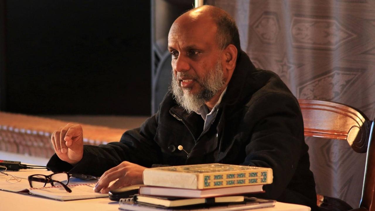 sits in conversation at a table with various writings and books (photo: Al-Salam Institute)