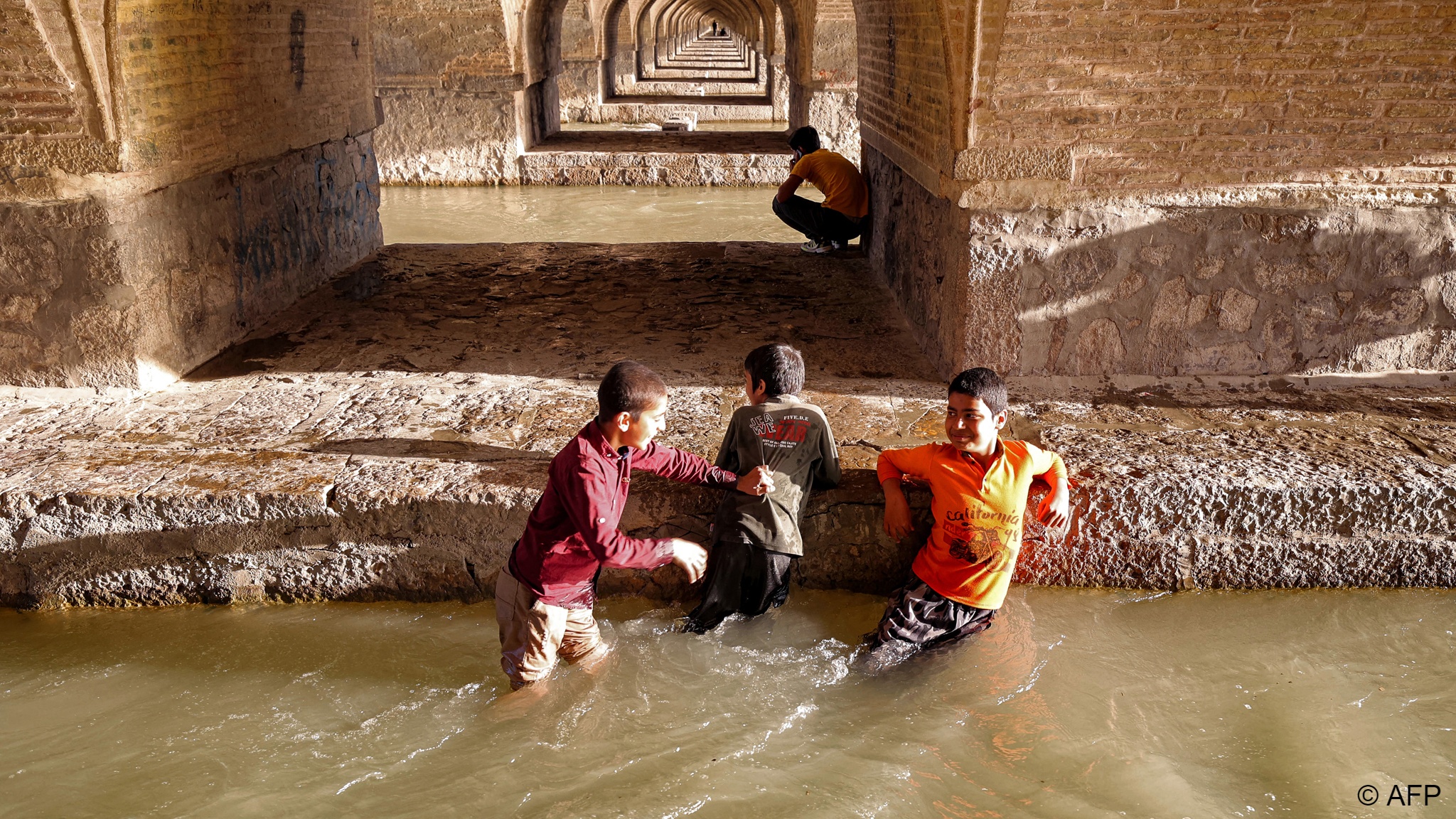 أولاد في مياه نهر زاينده تحت أقواس جسر. Boys wade in the water of the Zayandeh Rood beneath the arches of the Si-o-Se Pol bridge (photo: ATTA KENARE/AFP)