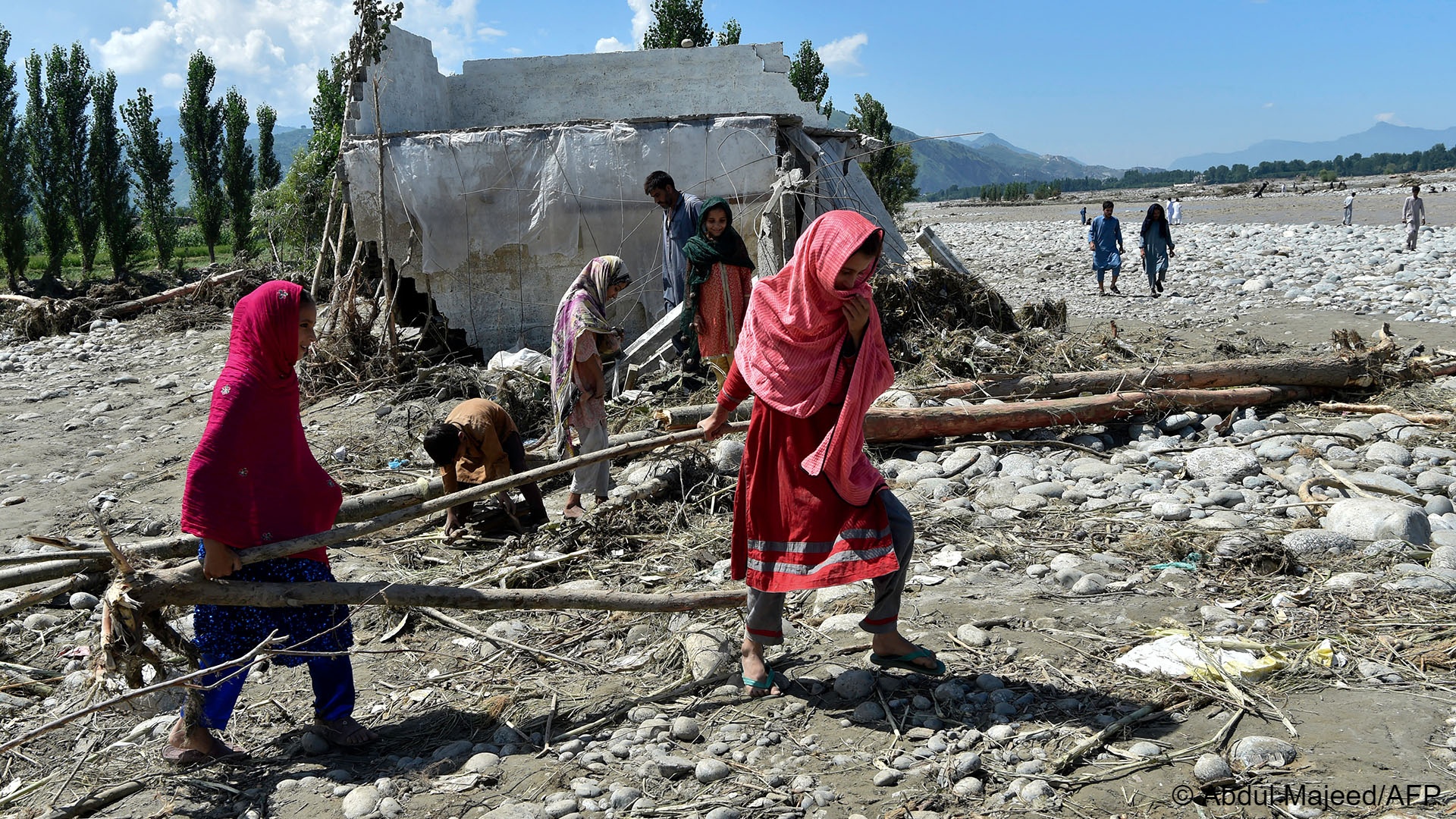 Girls carry wood near a damaged house along a river following heavy monsoon rains in Mingora, a town in Pakistan's northern Swat valley on August 28, 2022 (photo: Abdul MAJEED / AFP)