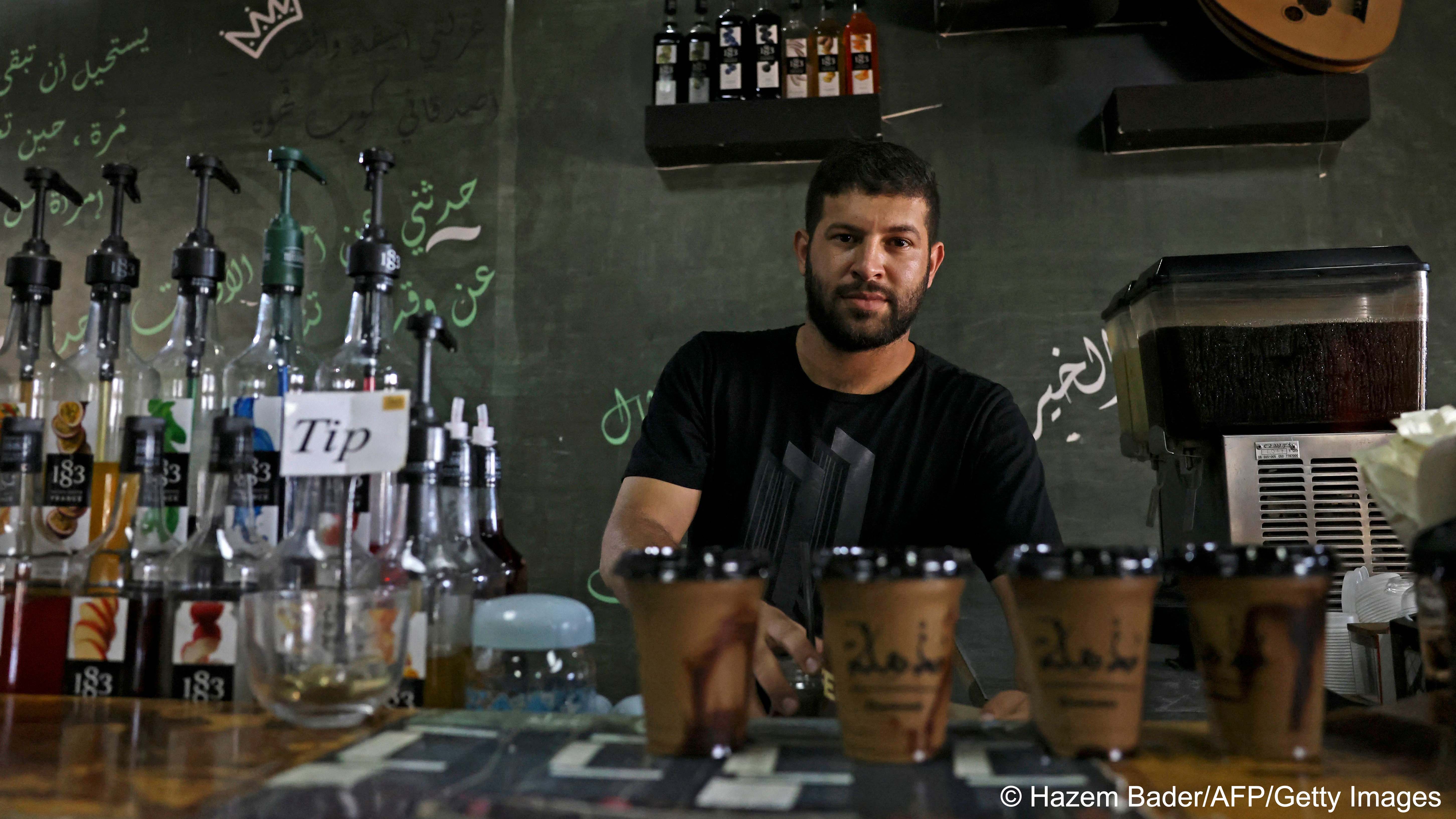 A man stands behind a bar with bottles and coffee beakers (photo: HAZEM BADER/AFP) 