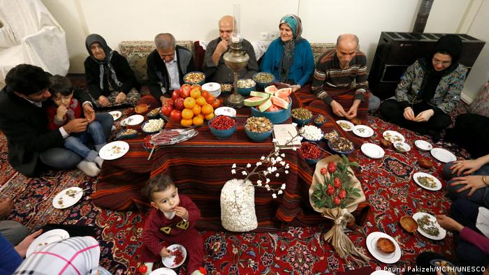 Eine Familie sitzt zum Fest Yalda mit Tellern um einen gedeckten Tisch auf dem Boden