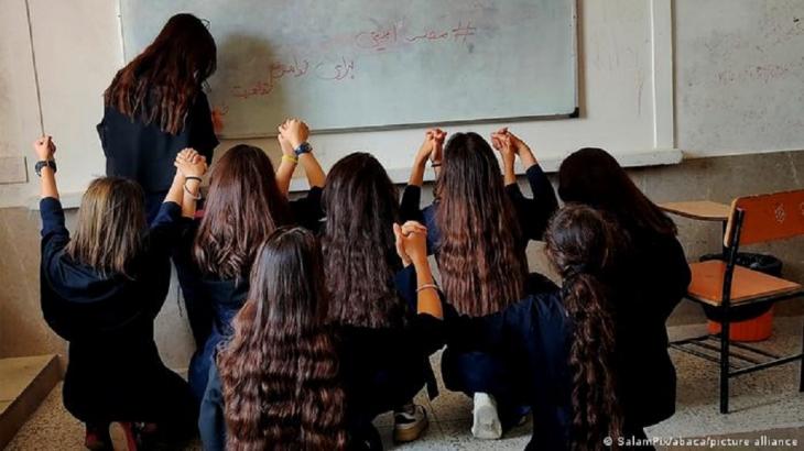 Young women without headscarves and with their backs to the camera raise their hands and look at a woman writing on a whiteboard (photo: SalamPix/abaca/picture alliance)