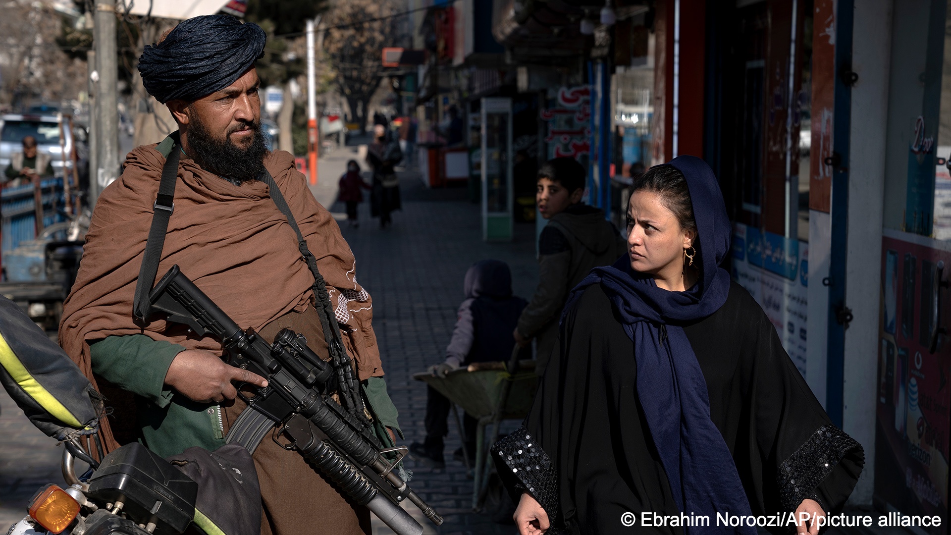 Ein Taliban-Kämpfer hält Wache, während eine Frau in Kabul vorbeigeht, Afghanistan, 26, Dezember 2022 (Ebrahim Noroozi/AP/picture alliance)