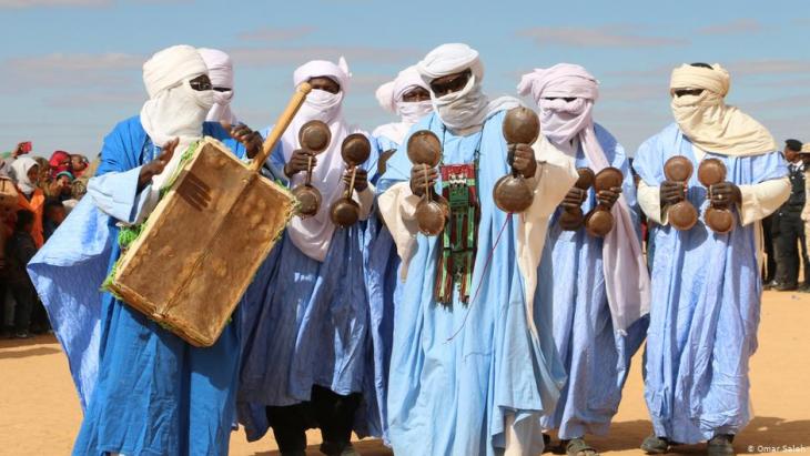 A group of seven traditional Tuareg musicians with veiled faces, dressed in blue robes and carrying musical instruments (photo: Omar Saleh)