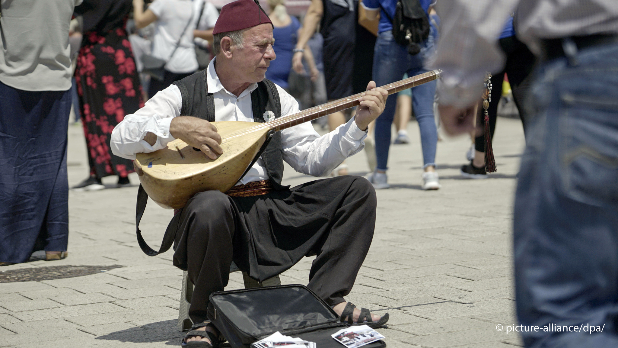 رجل يعزف عود الساز – تركيا. A man plays the baglama in the middle of a crowd in the sunshine (photo: picture alliance/dpa)