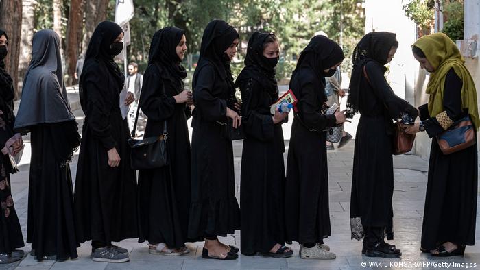 Eine Reihe junger Frauen, alle in langen schwarzen Gewändern und Kopftuch, stehen Schlange vor der Universität Kabul.