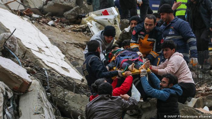 A chain of helpers lifts a stretcher with a person on it down from a pile of rubble