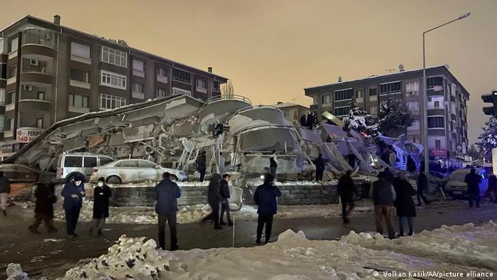 People stand around a collapsed building in a snowy city