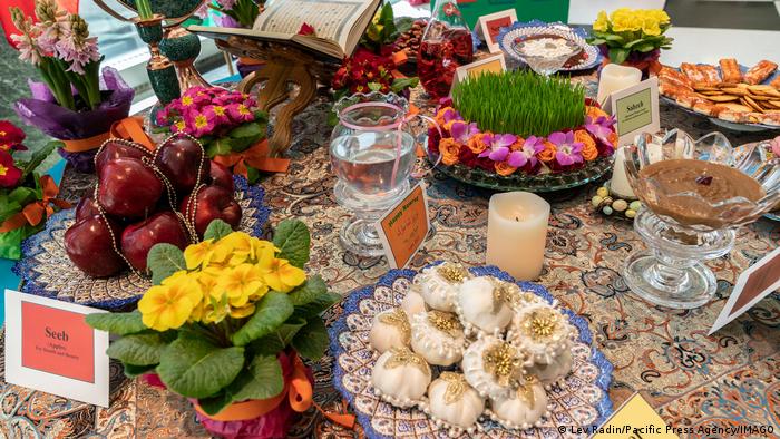A typical Nowruz table decorated for example with apples, garlic, flowers, a punch bowl with a live goldfish, a candle, with green grass and an open book.