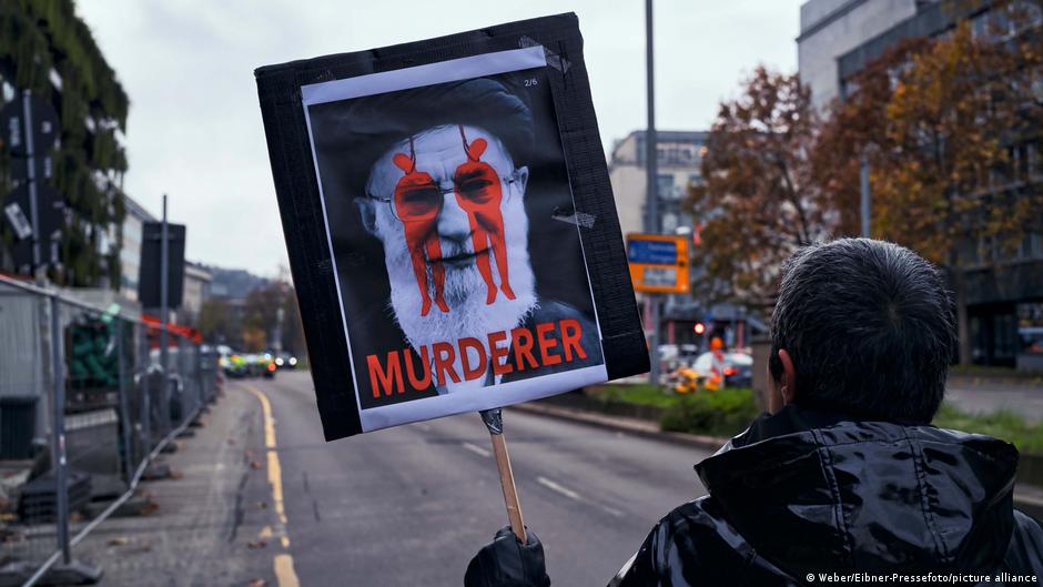 A protester in Berlin holds a placard with the word 'murderer' and an image of two hanged individuals superimposed over the face of Iran's supreme leader Ayatollah Ali Khamenei (image: Weber/Eibner-Pressefoto/picture alliance)