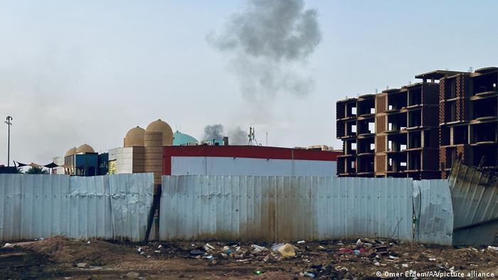 Smoke rises over buildings and a corrugated iron fence in Khartoum.