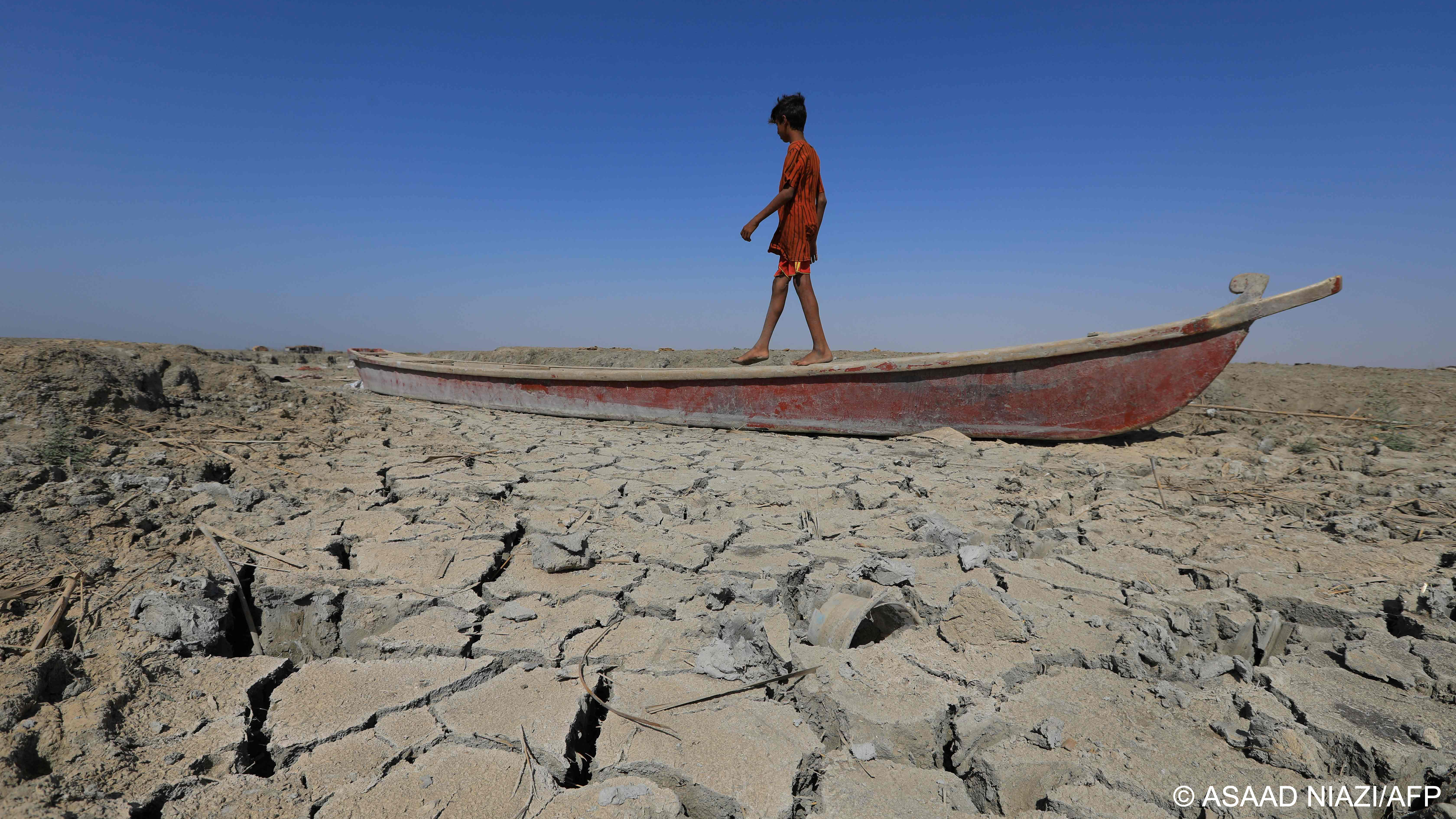 A boy walks on a boat on a dried-up section of the receding southern marshes of  Chibayish, Dhi Qar Governate, southern Iraq (photo: Asaad Niazi/AFP)