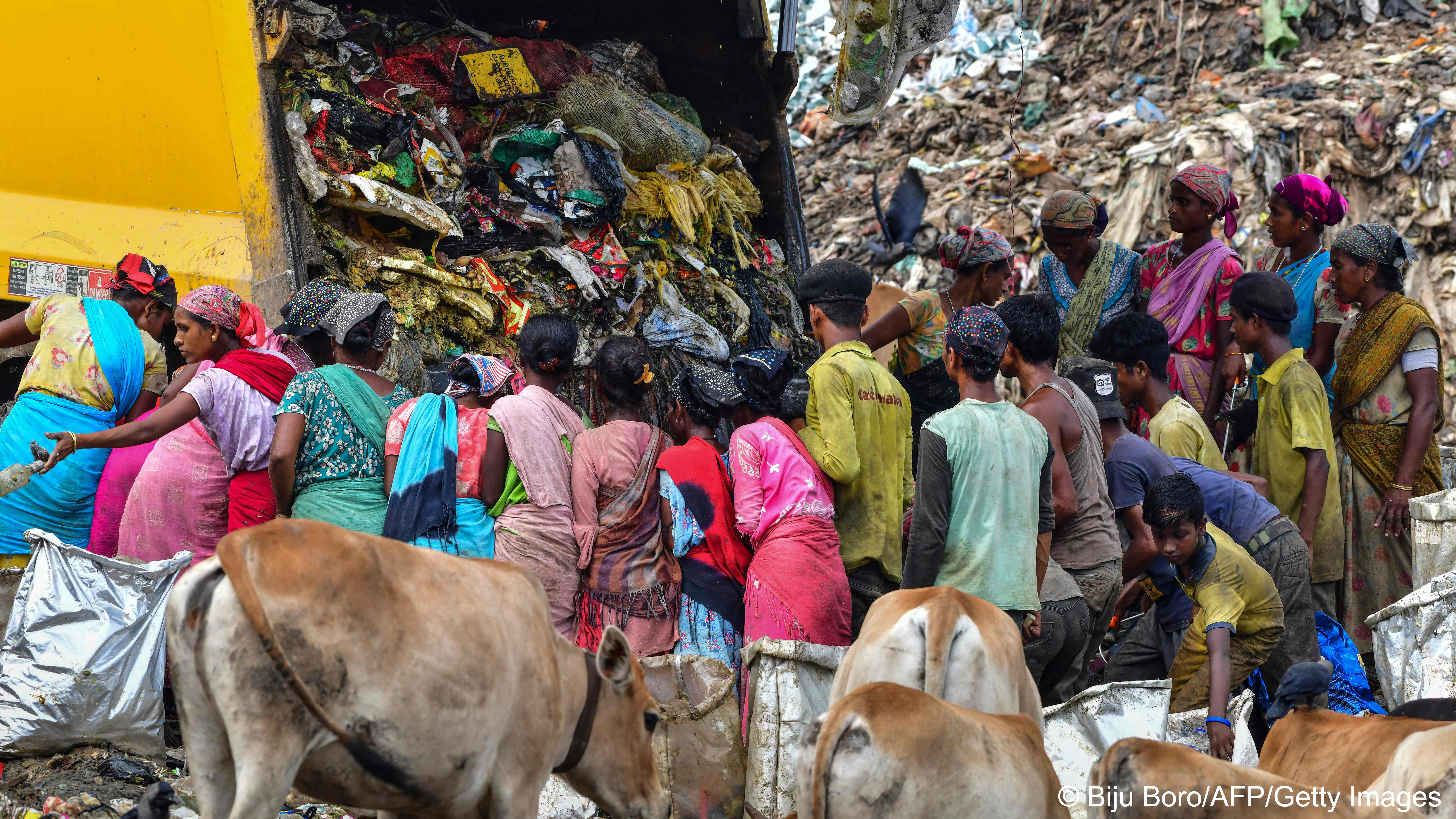 مجموعة من الناس يبحثون عن مواد قابلة للتدوير وإعادة الاستخدام في كومة ضخمة من القمامة - الهند. Ragpickers search for recyclable materials as a truck unloads garbage at a dumpsite in Guwahati on 2022 (image: Biju BORO/AFP)